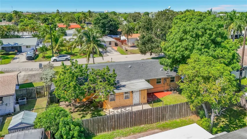 Single-story exterior featuring a shingle roof, concrete patio, perimeter wood fencing, and mature landscaping
