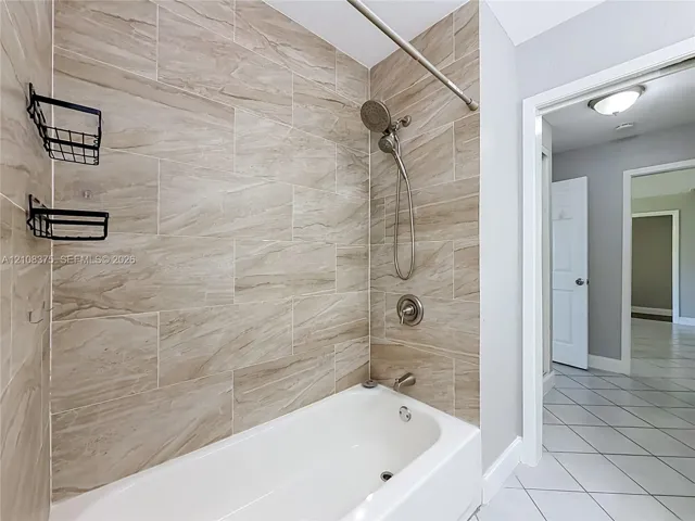 Bathtub and shower combination featuring large-format ceramic tile surround, brushed nickel hardware, and a handheld shower fixture