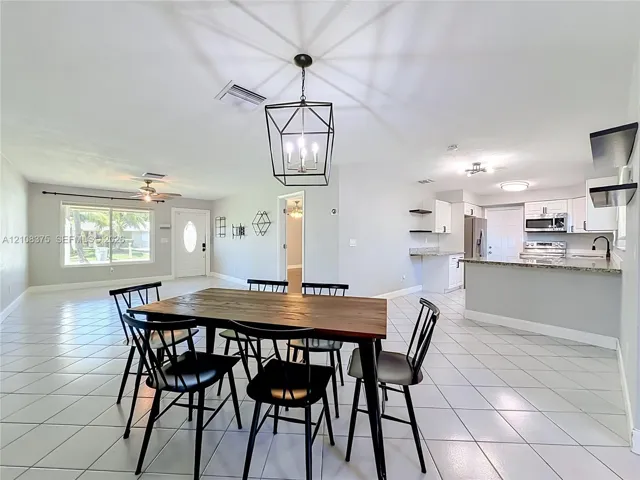 Open-concept interior featuring light-toned tile flooring, kitchen with peninsula counter, built-in cabinetry, and geometric lantern-style pendant lighting