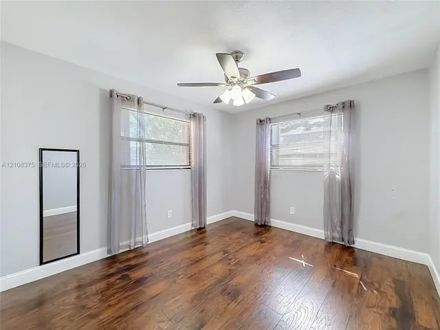 Wood-finish flooring, dual windows with horizontal blinds, and a central ceiling fan with integrated lighting