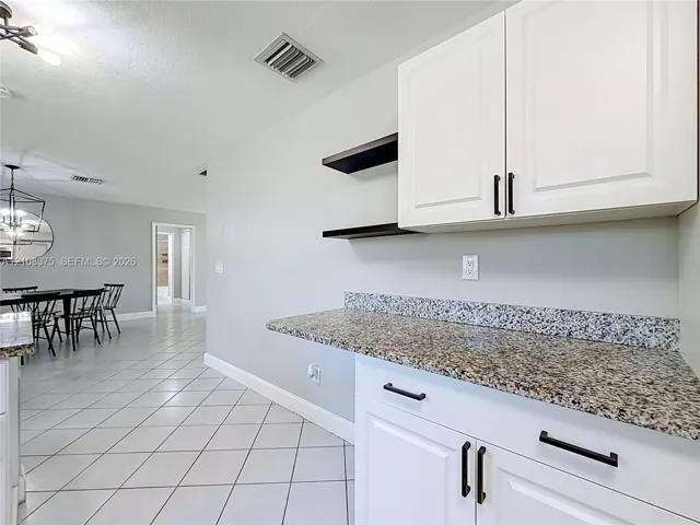 White cabinetry with matte black hardware, stone-finish countertops, floating shelving, and tile flooring