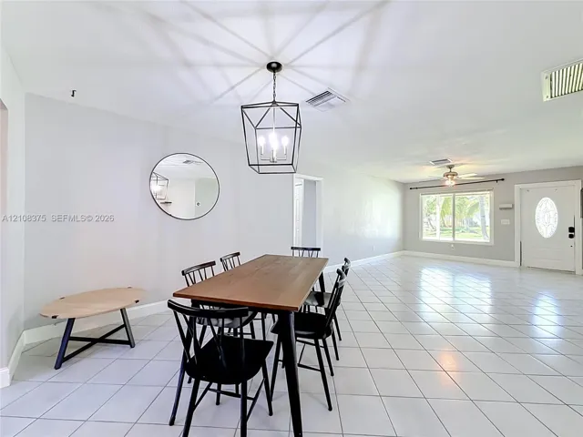 Large-format tile flooring, geometric metal cage pendant lighting, round wall mirror, and panel door with decorative glass insert