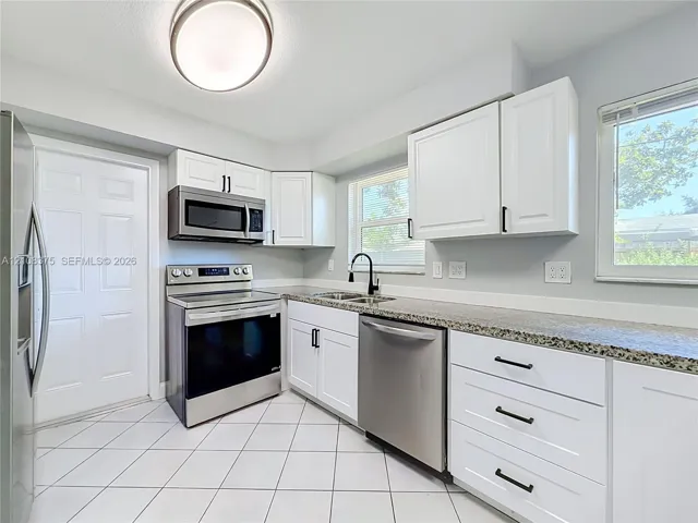 Kitchen featuring white shaker-style cabinetry, stone-finish countertops, stainless steel appliances, matte black hardware, and diagonal-set tile flooring