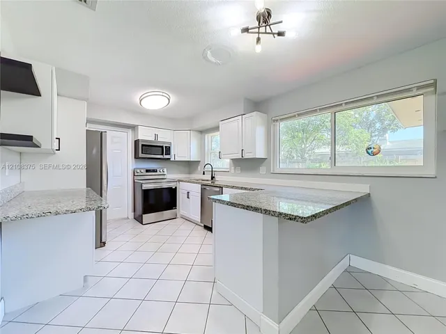 Kitchen featuring white cabinetry, stone-finish countertops, stainless steel appliances, a tile floor, and a multi-light chandelier
