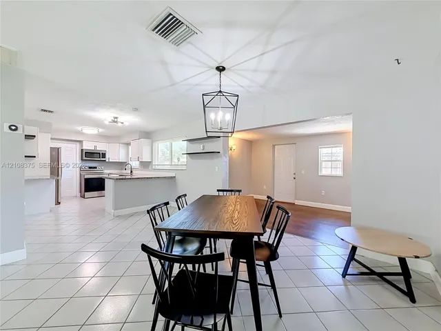 Open-concept floor plan featuring ceramic tile flooring, kitchen with white cabinetry, stone-finish countertops, stainless steel appliances, and a geometric metal pendant light fixture