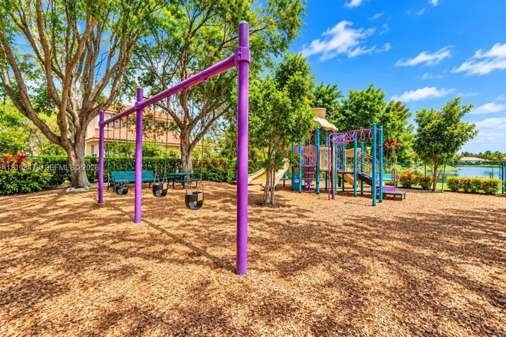 Recreational area featuring a multi-station playground structure, swing set, wood-chip ground cover, and mature trees