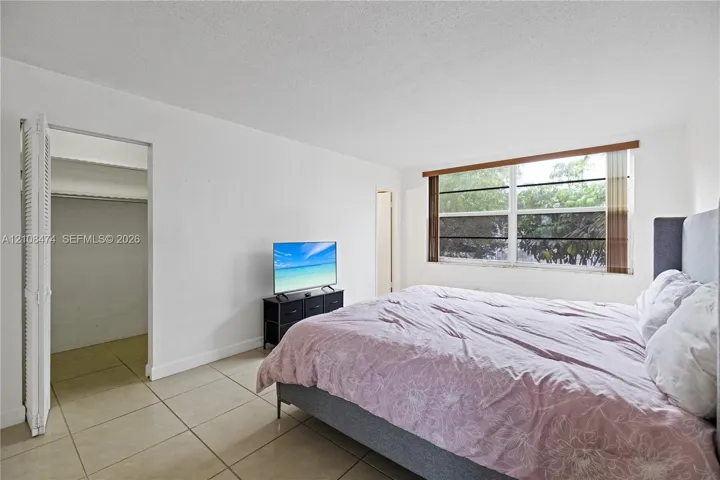 Neutral-toned tile flooring, large multi-pane window with wood-finish trim, and walk-in closet with bi-fold door