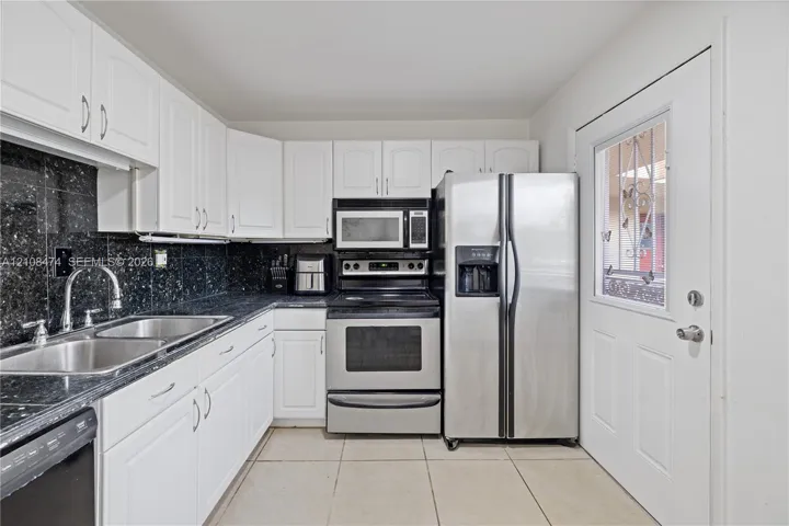 Kitchen featuring white cabinetry, dark stone-style countertops, tiled backsplash, stainless steel appliances, and tile flooring