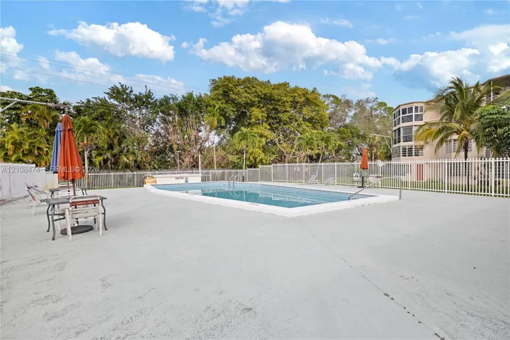 In-ground swimming pool featuring a concrete deck, perimeter fencing, and mature landscaping