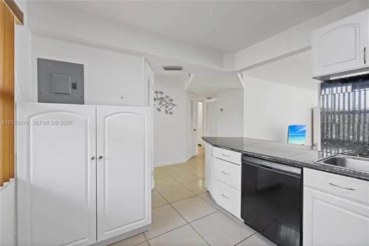 Kitchen featuring white shaker-style cabinetry, dark stone-finish countertops, tiled flooring, and a stainless steel built-in dishwasher