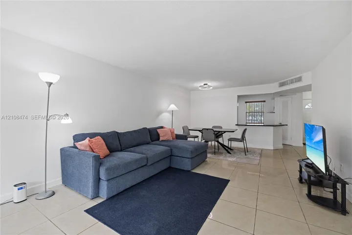 Open-concept interior featuring oversized tile flooring, a kitchen pass-through window with a breakfast bar, and recessed lighting