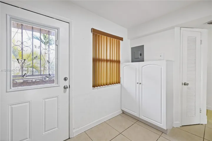 Exterior door with decorative security grating, tile flooring, built-in cabinetry, and louvered closet door