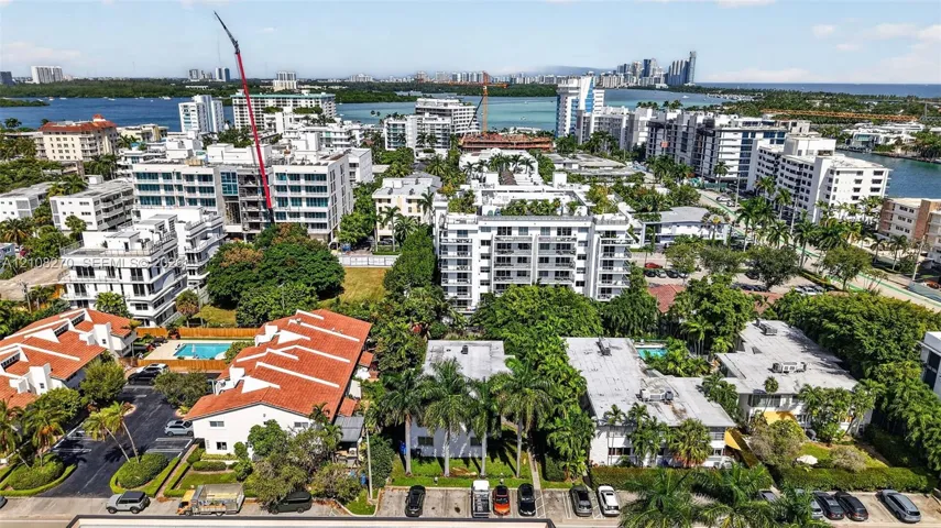 Aerial perspective of a multi-residential enclave featuring orange-tiled rooflines, manicured palm landscaping, asphalt surface parking, and perimeter hedging