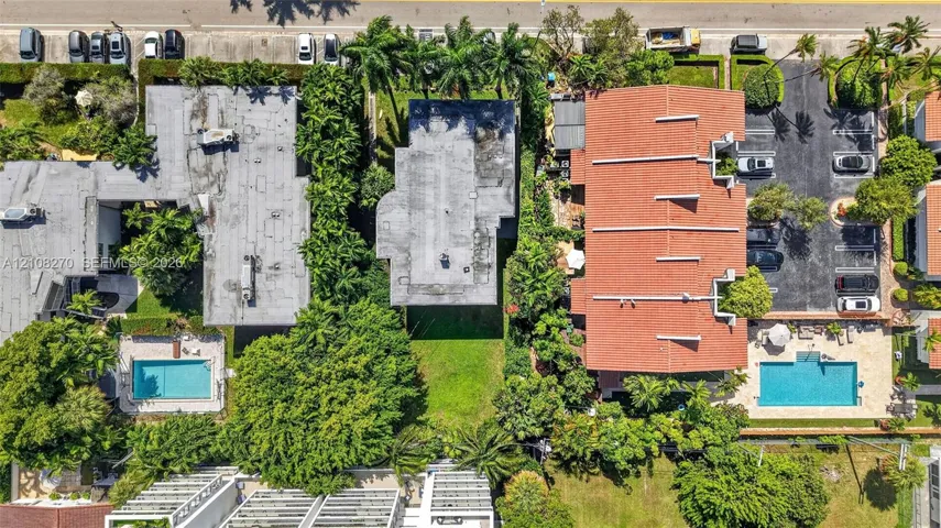 Aerial perspective showcasing a parcel of land with established green space, mature canopy trees, lush landscaping, and integrated paved parking