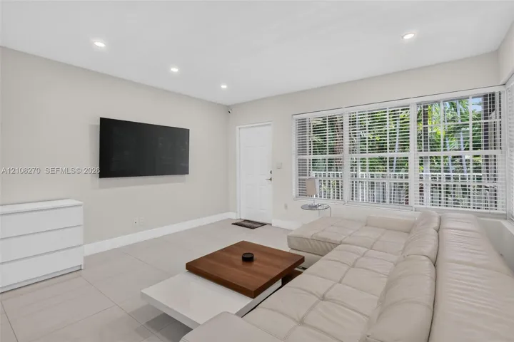 Neutral-toned interior featuring large-format ceramic tile flooring, recessed lighting, and expansive multi-pane windows with horizontal blinds