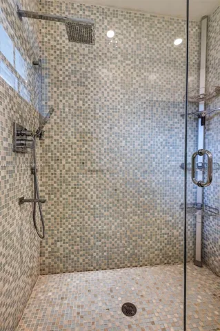Walk-in shower featuring glass enclosure, mosaic tile wall surround, rainfall showerhead, handheld sprayer, and built-in corner shelving