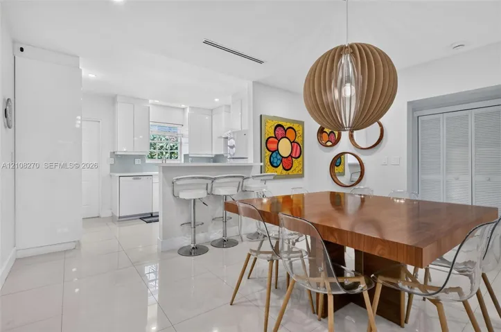 Kitchen featuring high-gloss cabinetry, stone-finish countertops, porcelain tile flooring, and a breakfast bar, complemented by a statement spherical wood-slat pendant light