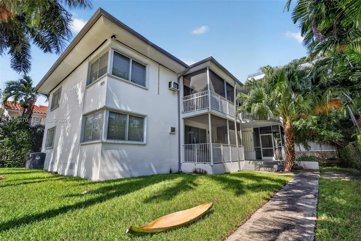 Two-story exterior featuring a white stucco facade, multi-level screened-in balconies with white metal railings, horizontal sliding windows, and a paved walkway