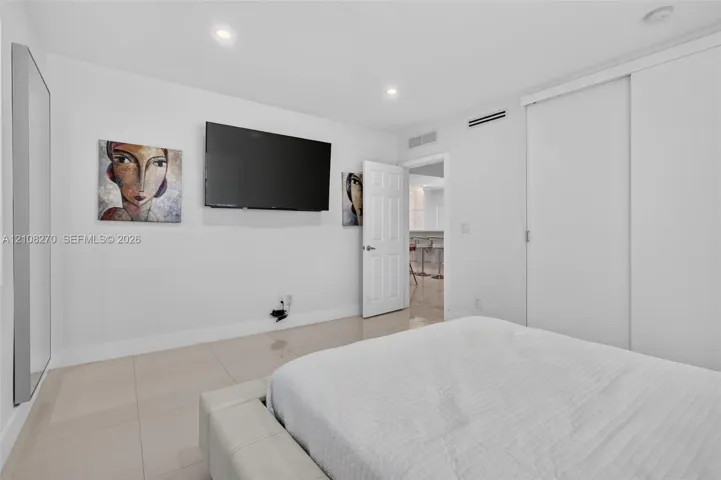 Neutral-toned tile flooring, recessed ceiling lighting, and sliding closet doors with white finish