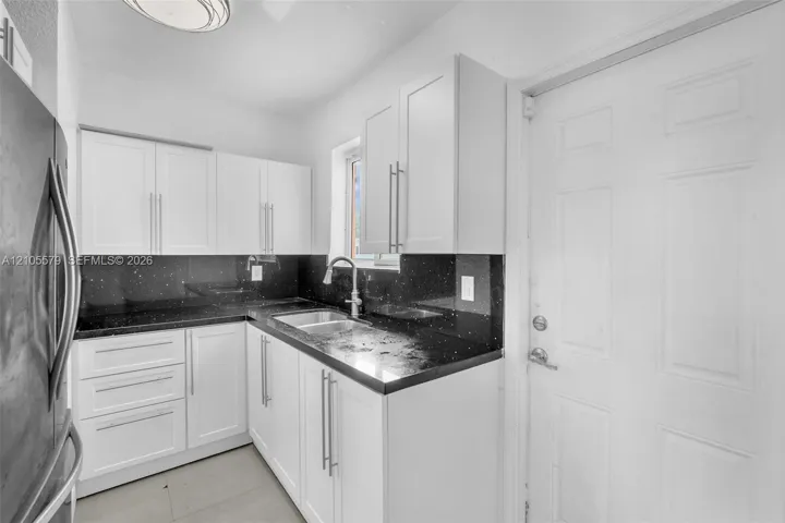 Kitchen featuring white shaker-style cabinetry, dark stone-finish countertops, stainless steel dual-basin sink with pull-down faucet, and sleek metallic hardware