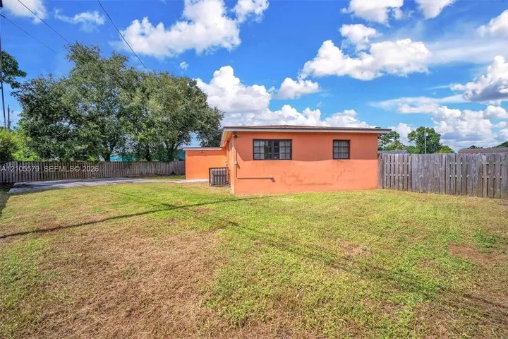 Exterior of the residence featuring a concrete masonry unit wall finish, rectangular grid windows, and an expansive rear yard enclosed by wooden perimeter fencing