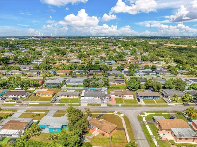 Aerial perspective of the residential property featuring a paved driveway, a multi-car garage, an enclosed rear patio, and mature landscaping