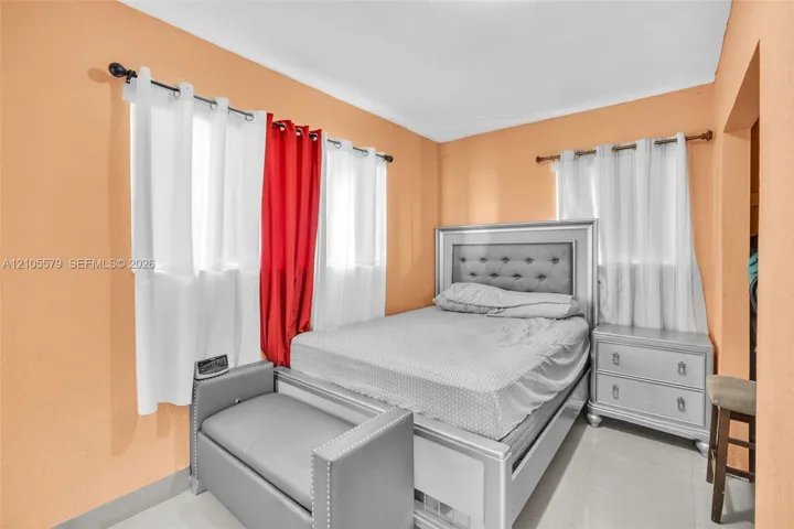 Bedroom with dual-aspect windows, white-finished rod hardware, and light-colored tile flooring