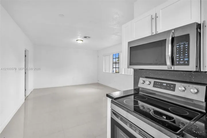 Kitchen featuring white shaker-style cabinetry, a stainless steel microwave, and a glass-top electric range with a dark solid-surface countertop