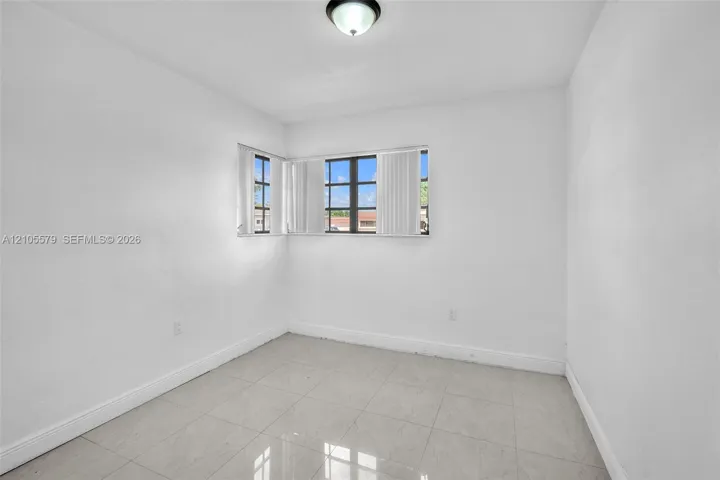 Neutral interior space featuring polished tile flooring, smooth white walls, corner-positioned multi-pane windows, and a flush-mount ceiling fixture