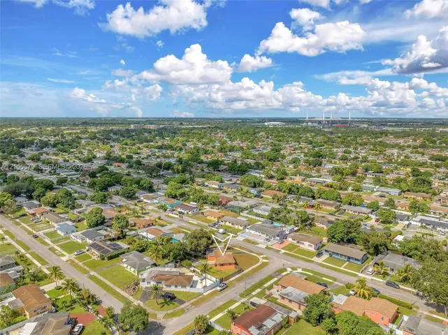 Aerial perspective of a single-story residence situated on a corner lot featuring a fenced rear perimeter, mature landscaping, and an asphalt-shingled roof