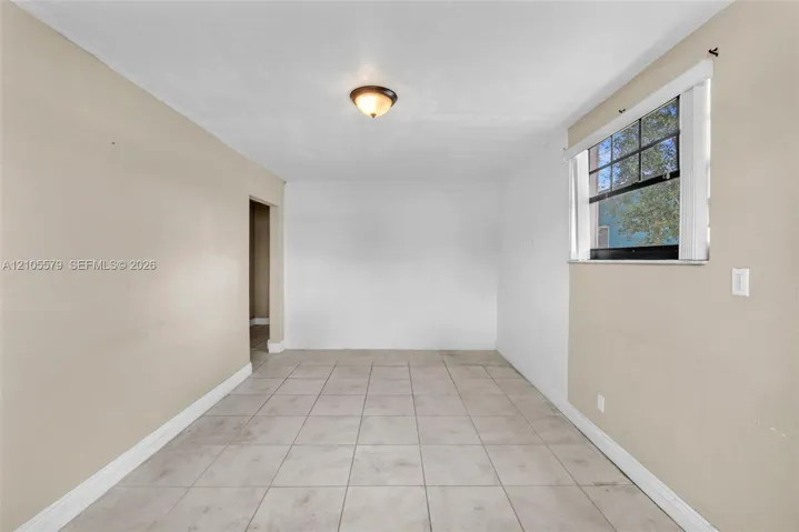 Neutral-toned interior space featuring light-colored tile flooring, smooth walls, a single-pane window with dark muntins, and a flush-mount ceiling light fixture