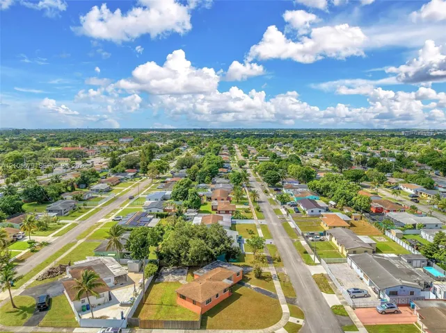 Aerial perspective of the property featuring a corner lot, established landscaping, mature palm trees, and residential street frontage