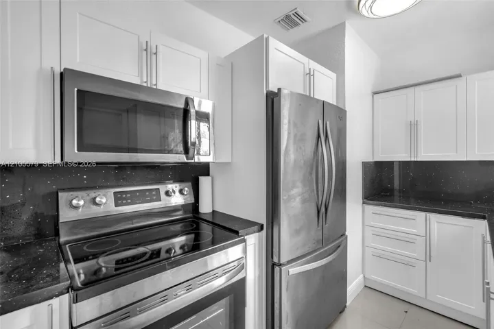 Kitchen featuring white shaker-style cabinetry, stainless steel appliances, dark stone countertops, and a glass cooktop range