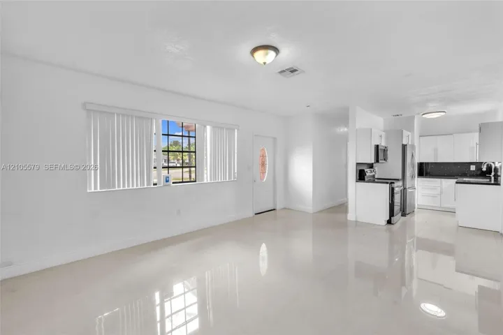 Open floor plan featuring polished tile flooring, recessed and flush-mount ceiling lighting, window with vertical blinds, and a kitchen equipped with white cabinetry and dark countertops