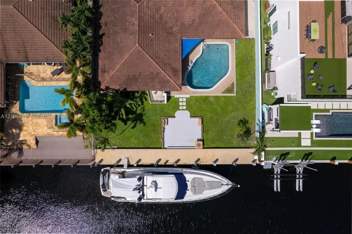 Waterfront property featuring a private concrete dock, an in-ground swimming pool, a sodded lawn, and a paved patio area