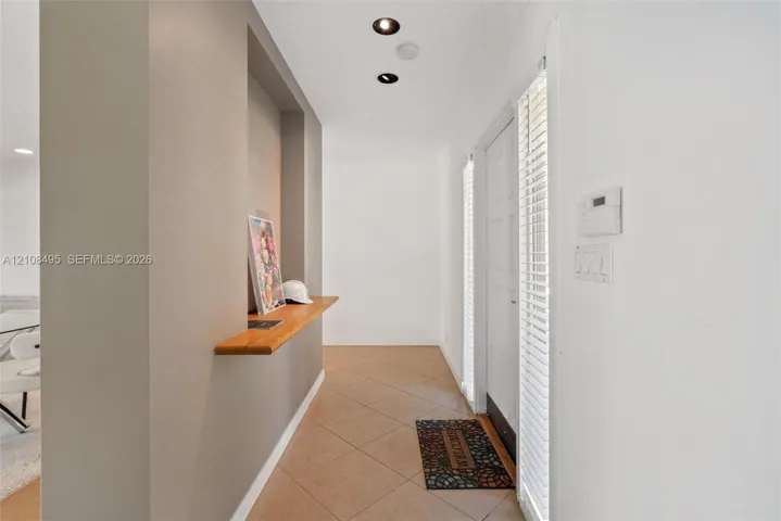 Entryway featuring a built-in wood-finish display shelf, recessed ceiling lighting, tile flooring, and vertical blinds