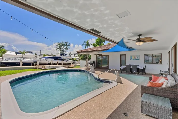 Covered outdoor patio with a ceiling fan, concrete pool deck, and an inground swimming pool with water access