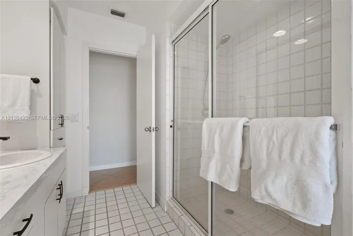 Bathroom featuring a vanity with a white countertop and integrated sink, a glass-enclosed shower with tiled surround, and a tall built-in storage cabinet with matte black hardware