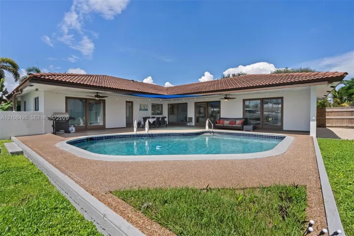 L-shaped exterior featuring a tiled roof, in-ground swimming pool with aggregate decking, and multiple sliding glass door entries