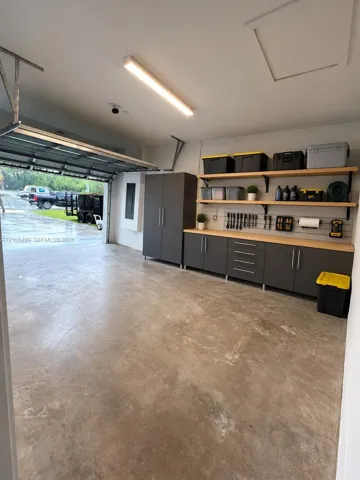 Garage featuring custom floor-to-ceiling cabinetry, integrated wall-mounted slat organization, wood-surfaced built-in workbench, and overhead linear lighting