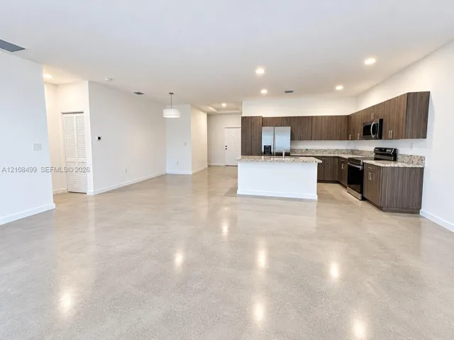 Polished concrete flooring, recessed lighting, horizontal wood-grain cabinetry, stone-surface countertops, and built-in stainless steel appliances