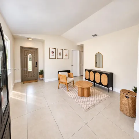 Entryway featuring large-format neutral floor tile, vaulted ceilings, and a paneled front door with decorative glass inlay