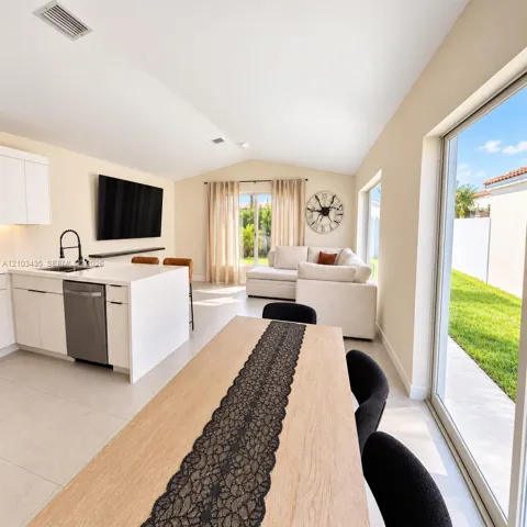 Open-concept interior featuring light-toned cabinetry, a stone-surface kitchen island with a matte black faucet, vaulted ceilings, and large sliding glass doors providing access to the exterior