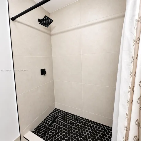 Shower featuring large-format neutral wall tile, black hexagon floor tile, matte black rain-style shower head, and matte black single-handle mixing valve