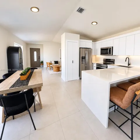 Modern kitchen featuring a waterfall-edge stone island, white flat-panel cabinetry, stainless steel appliances, and large-format tile flooring