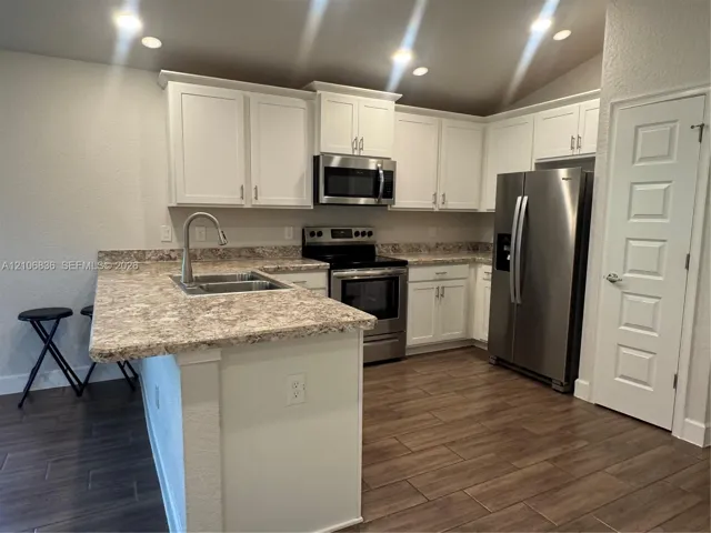 Kitchen featuring white cabinetry, stone-patterned countertops, stainless steel appliances, a high-arc kitchen faucet, and wood-finish tile flooring