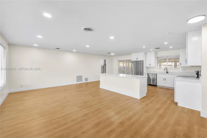 Open-concept interior featuring wood-finish flooring, recessed lighting, and a kitchen equipped with white cabinetry, quartz countertops, and a stainless steel refrigerator