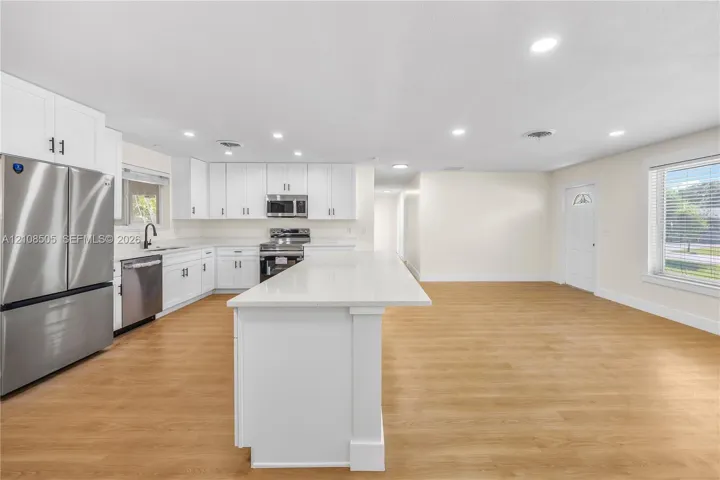 Kitchen featuring white cabinetry, an expansive central island with a solid-surface countertop, stainless steel appliances, and wood-finish flooring with recessed lighting