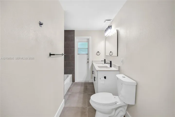 Dual-vanity cabinetry with rectangular integrated sinks, matte black fixtures, neutral large-format floor tiling, and a tub enclosure with full-height tile surround