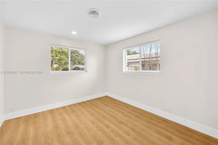 Neutral interior space featuring wood-finish flooring, dual windows with horizontal blinds, and recessed ceiling lighting